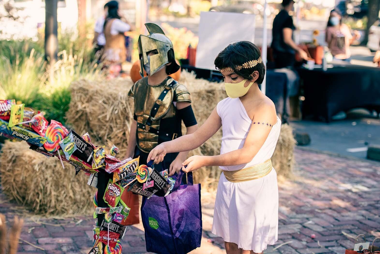 Two children in costumes are standing next to each other at a trick or treat event.