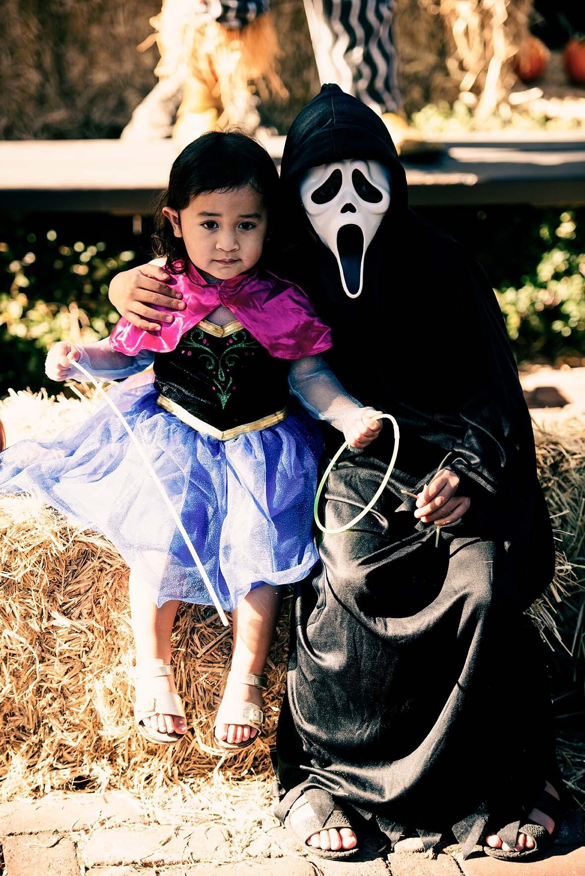 A little girl is sitting next to a person dressed as scream