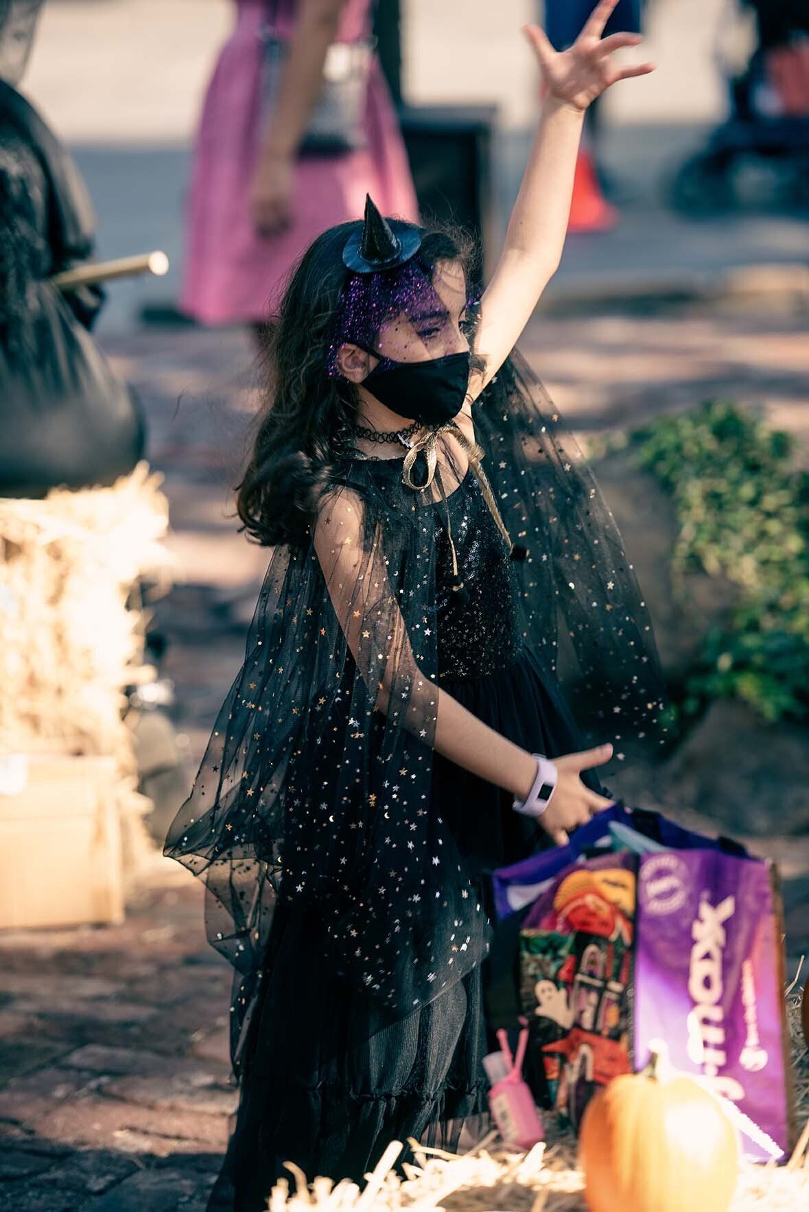 A little girl in a halloween costume is wearing a mask and holding a trick or treat bag.