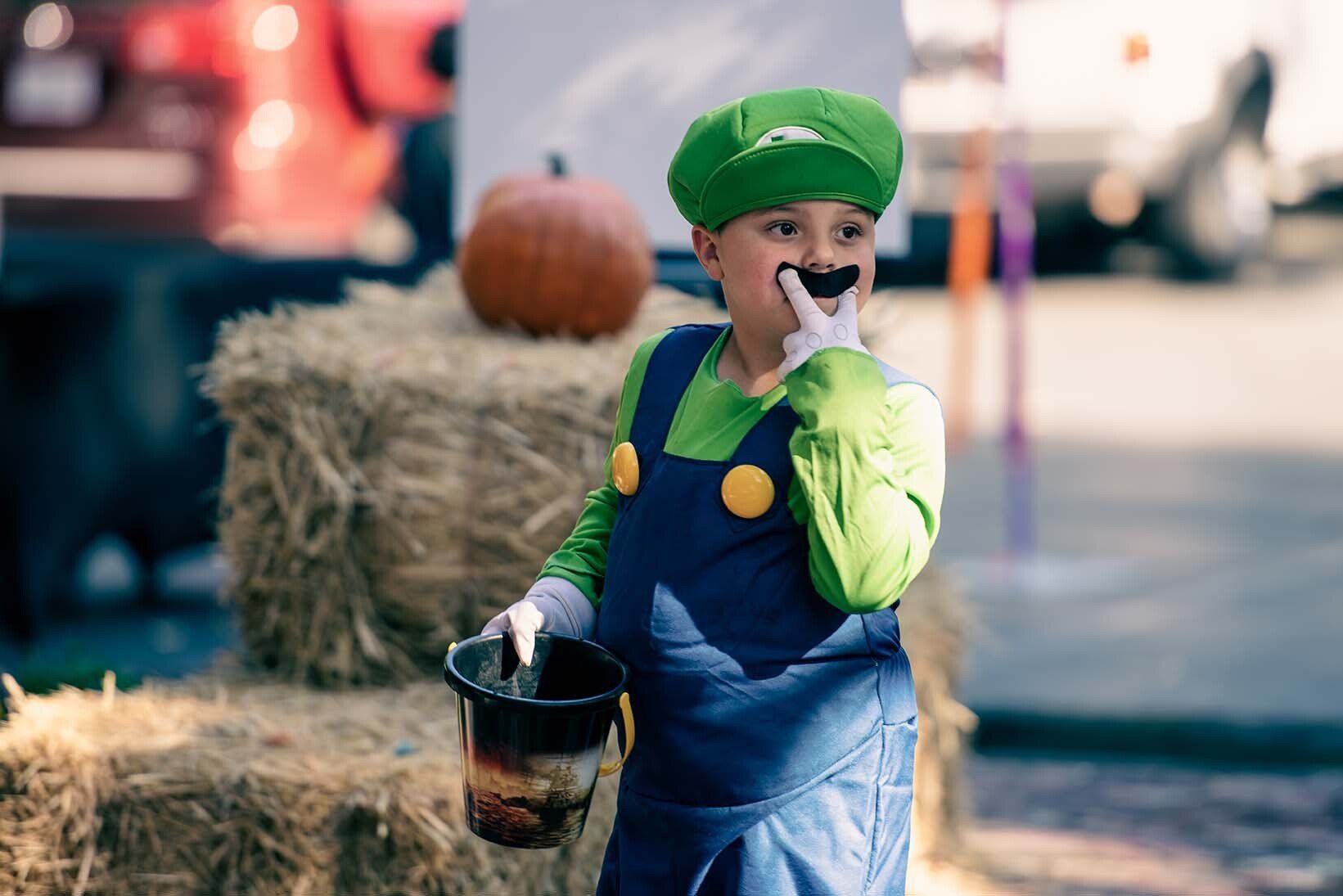 A young boy in a mario costume is holding a bucket of treats.
