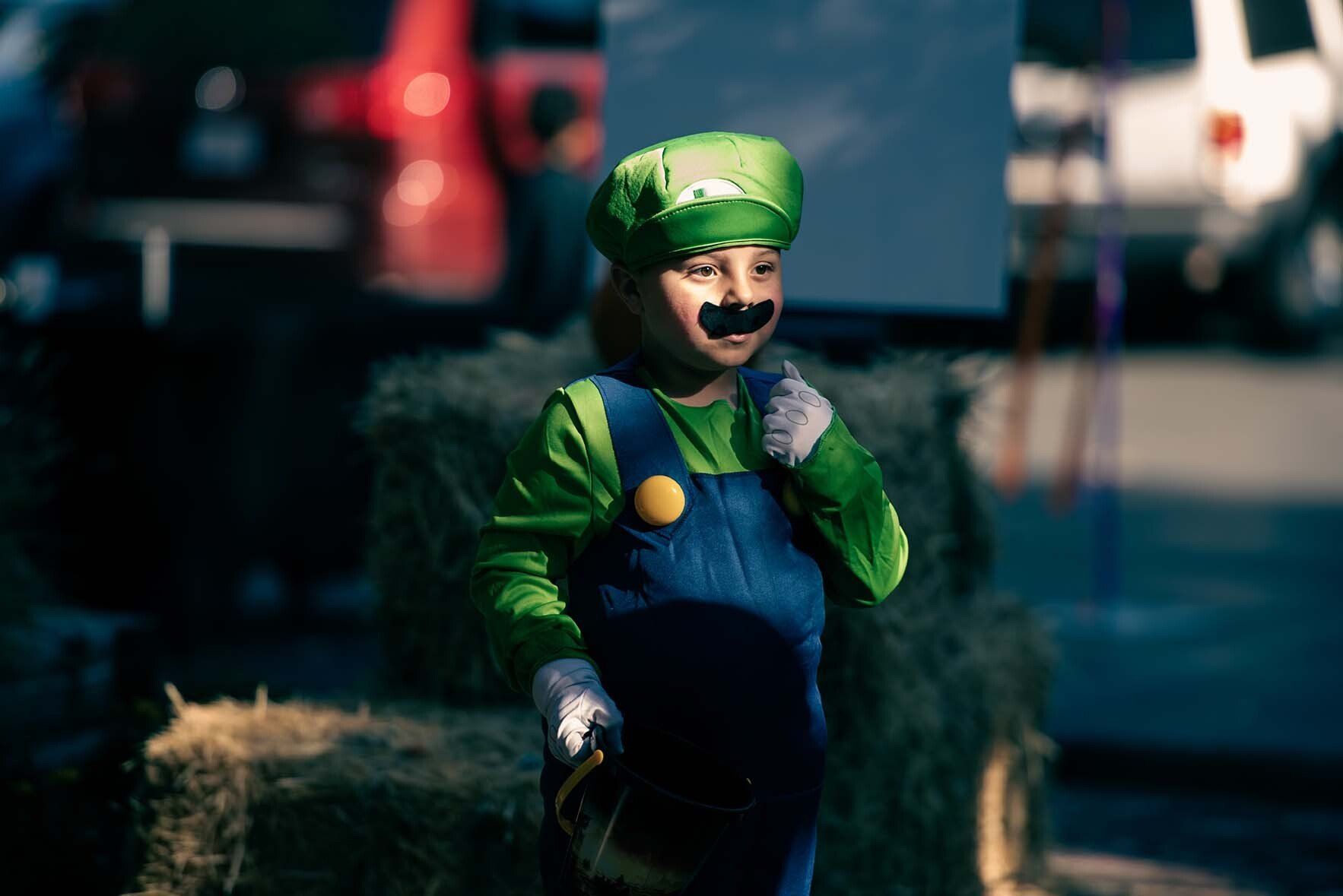 A young boy in a luigi costume is standing in front of hay bales.