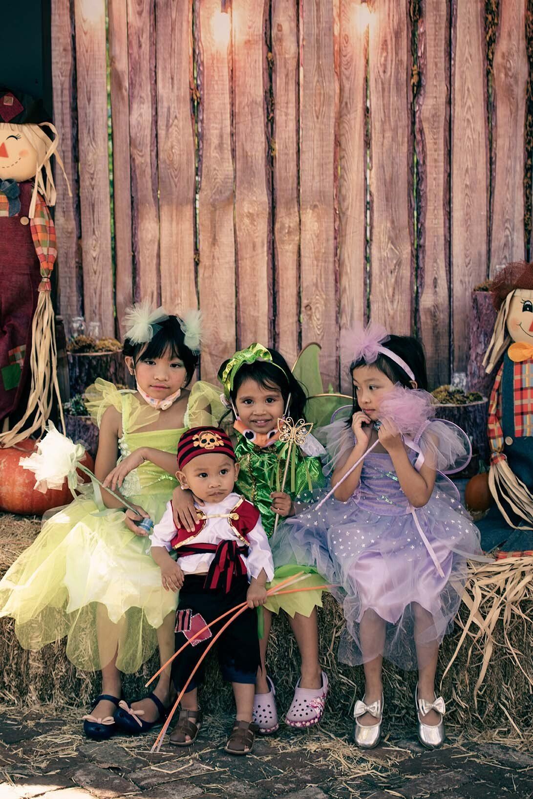 A group of children in halloween costumes are sitting on hay bales.