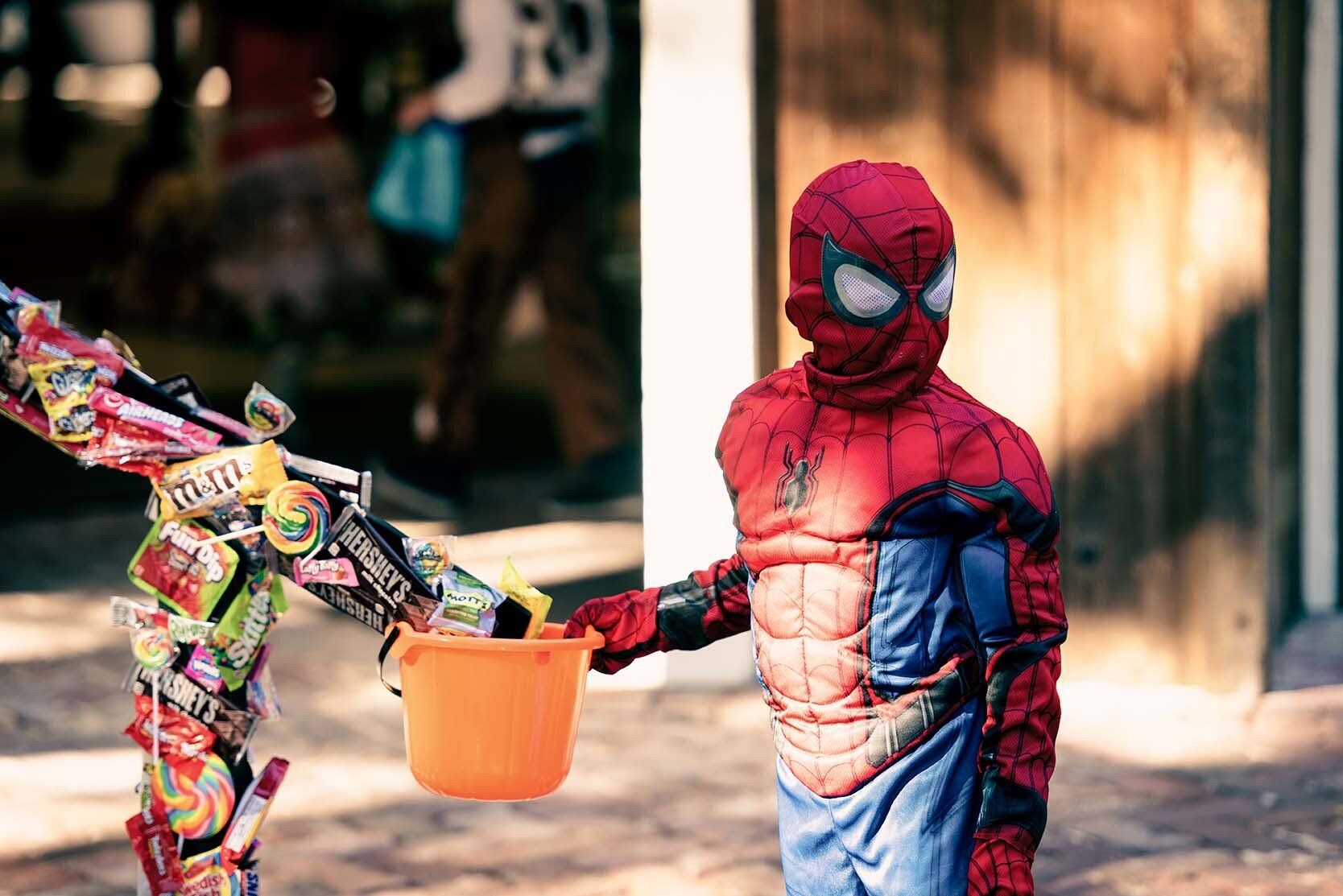 A child in a spiderman costume is giving candy to another child.