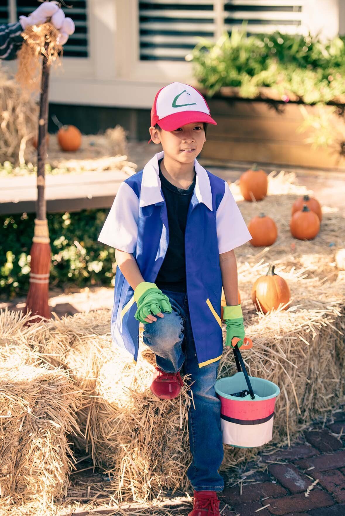 A young boy in a pokemon costume is sitting on a bale of hay holding a bucket.