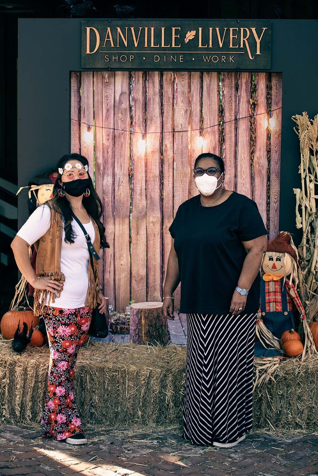 Two women wearing face masks are standing next to each other in front of a wooden wall.