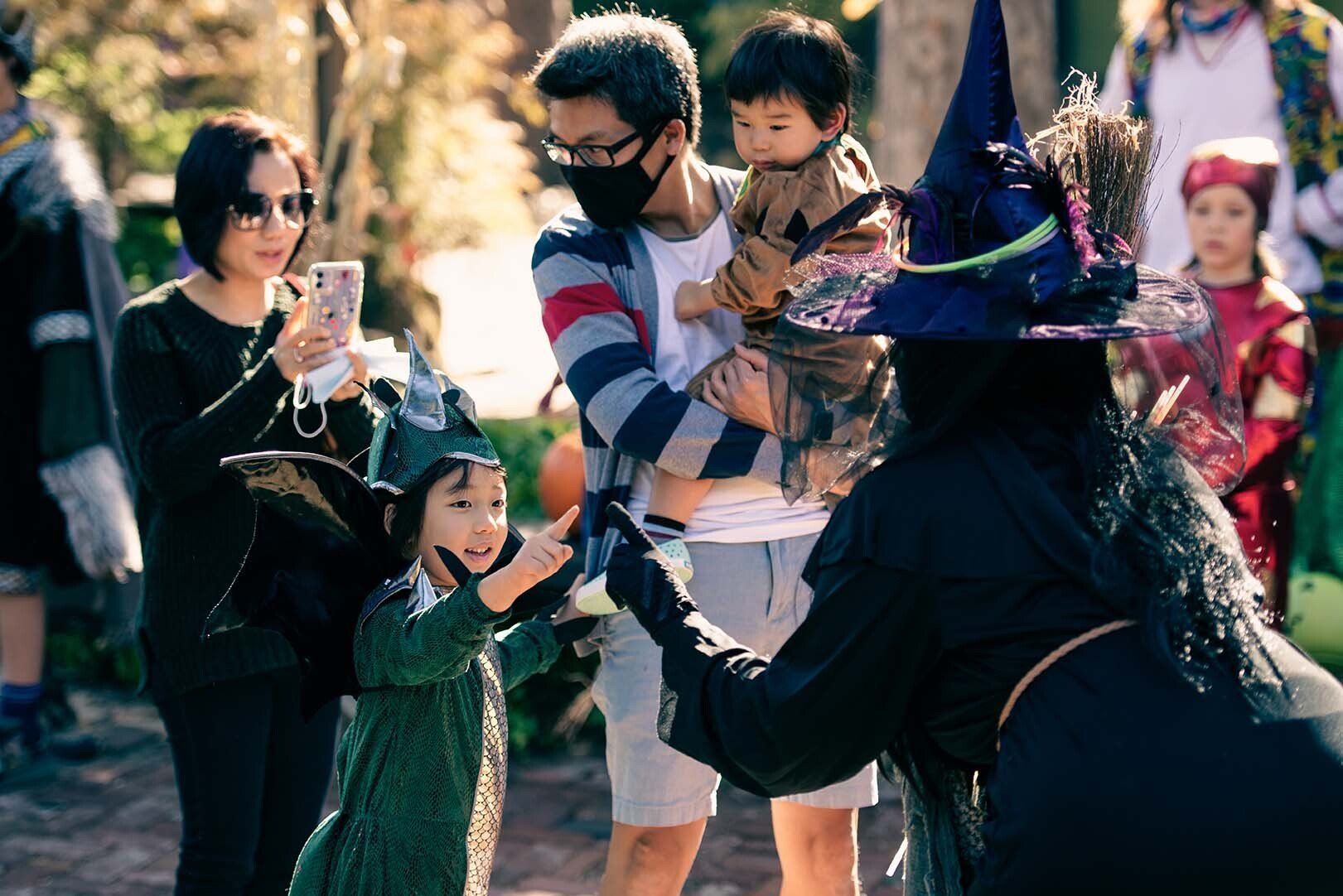 A woman in a witch costume is talking to a little girl.