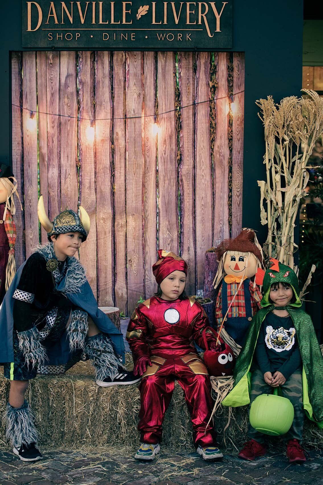 A group of children in halloween costumes are sitting on hay bales.