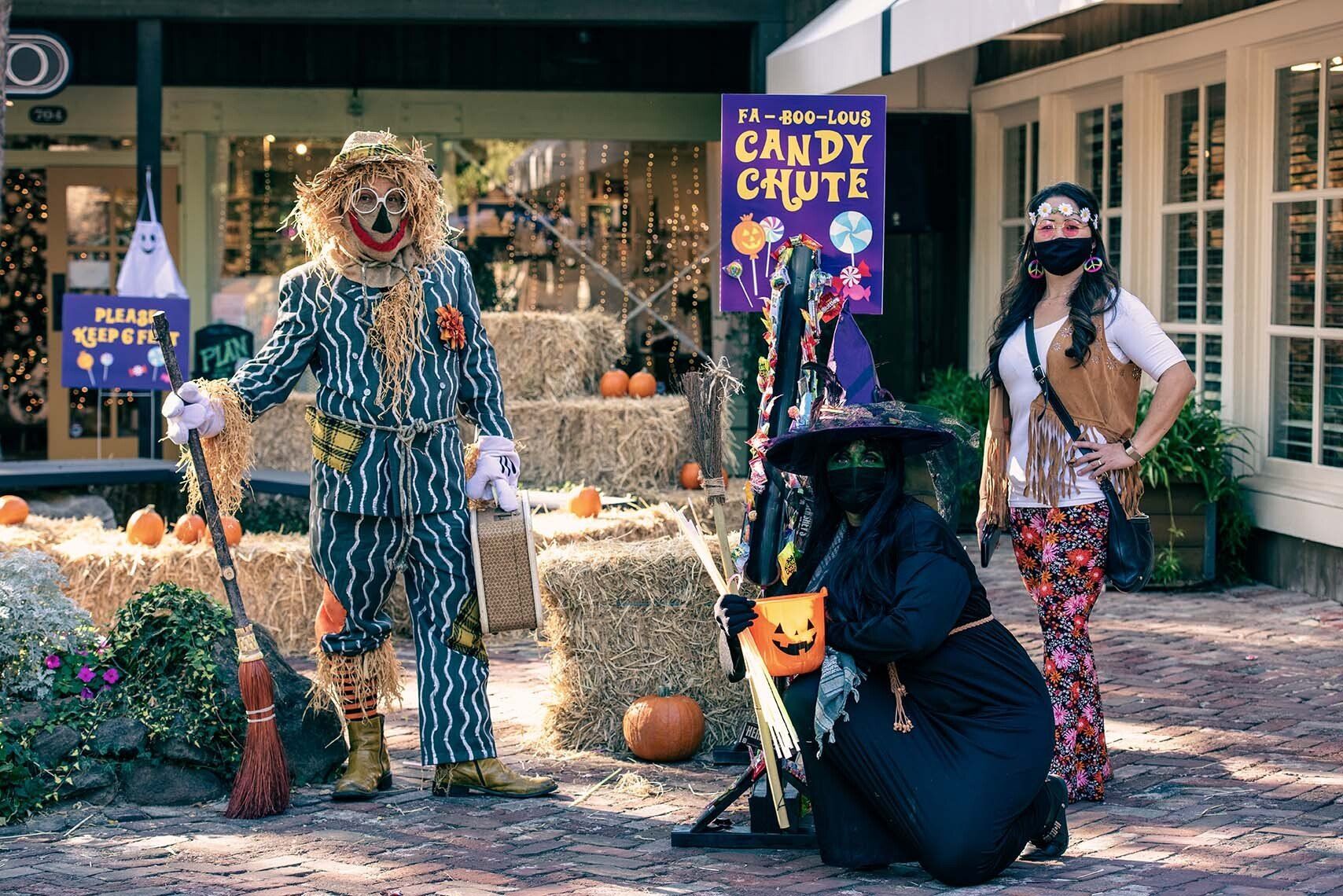 A scarecrow and a witch are standing in front of a sign that says candy chute