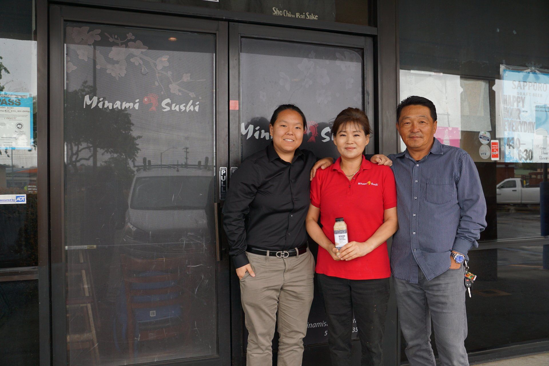 Three people are posing for a picture in front of a sushi restaurant.