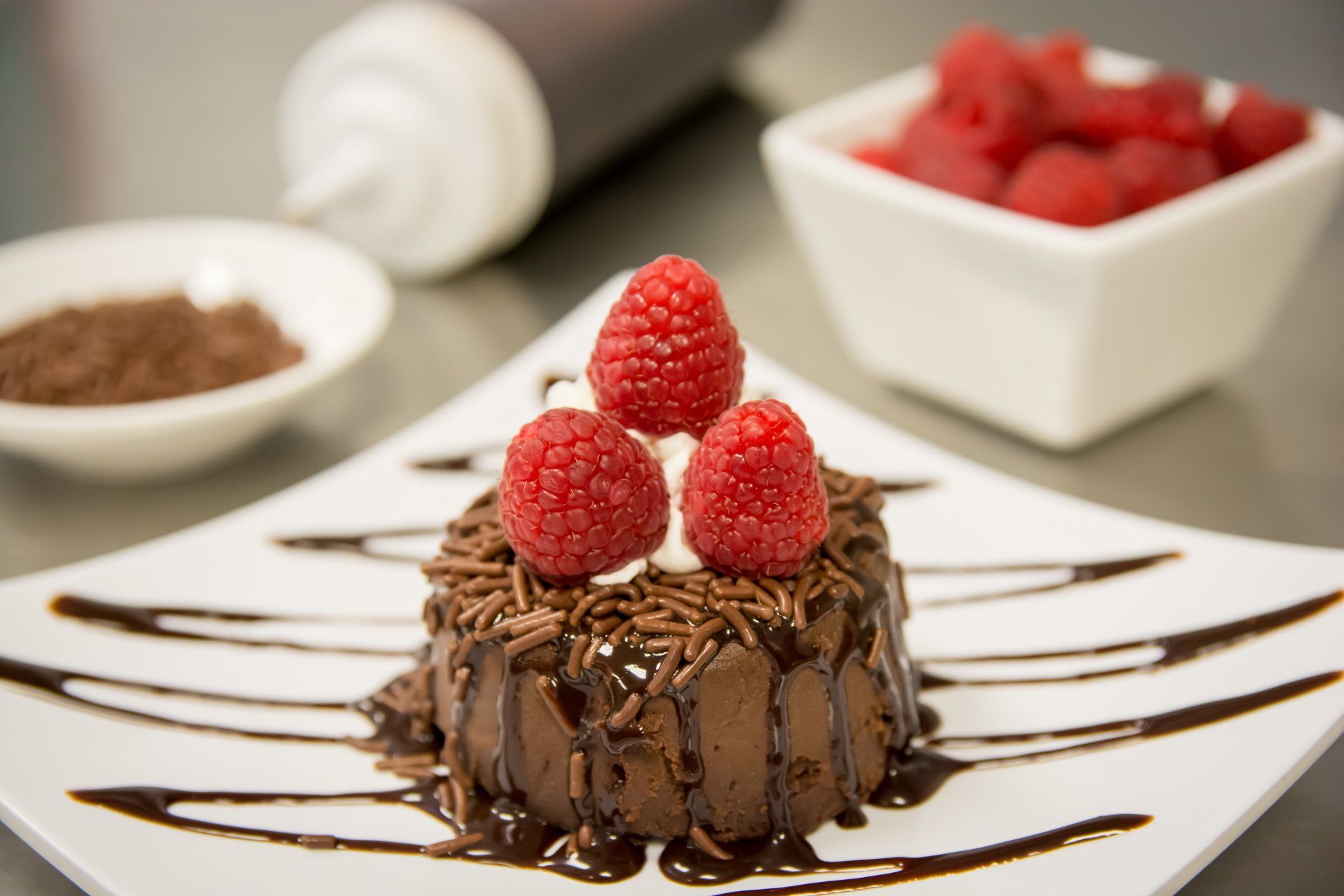 A chocolate dessert with raspberries on top on a white plate