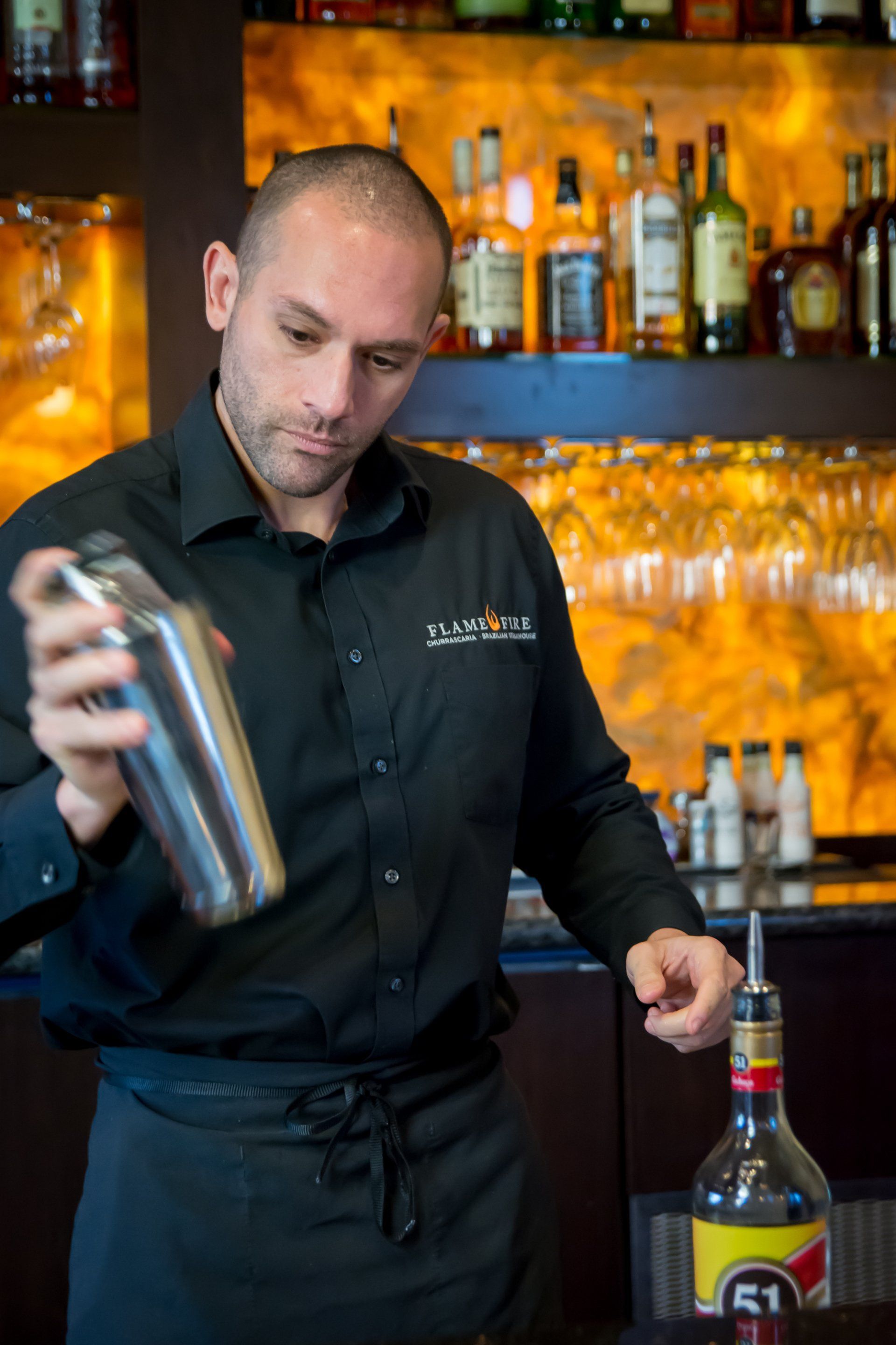 A man in a black shirt is shaking a drink in a bar.