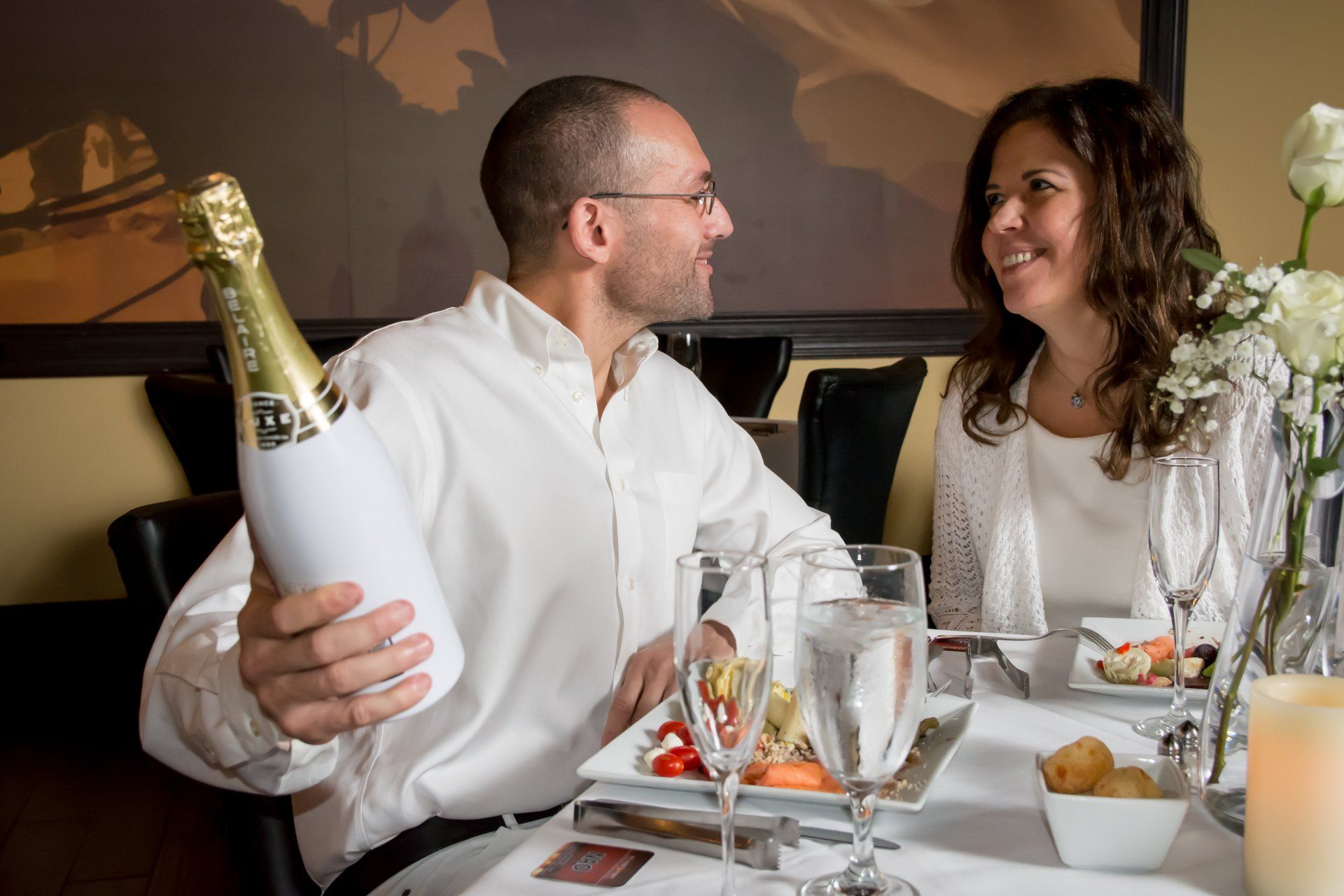 A man is holding a bottle of champagne while sitting at a table with a woman.