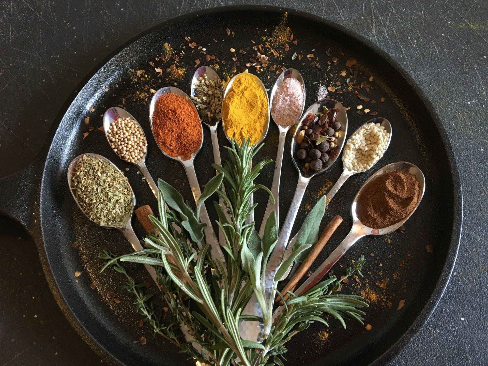 A black plate topped with spoons filled with different spices and herbs.