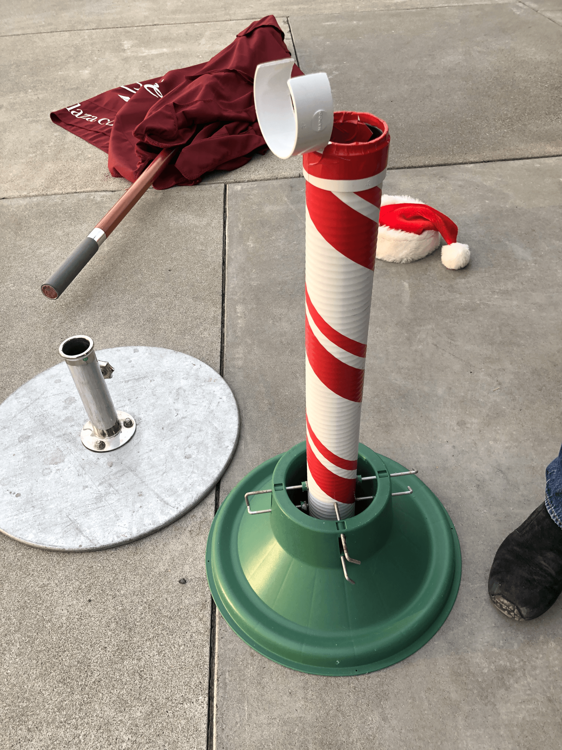 A candy cane is sitting on the ground next to a santa hat.