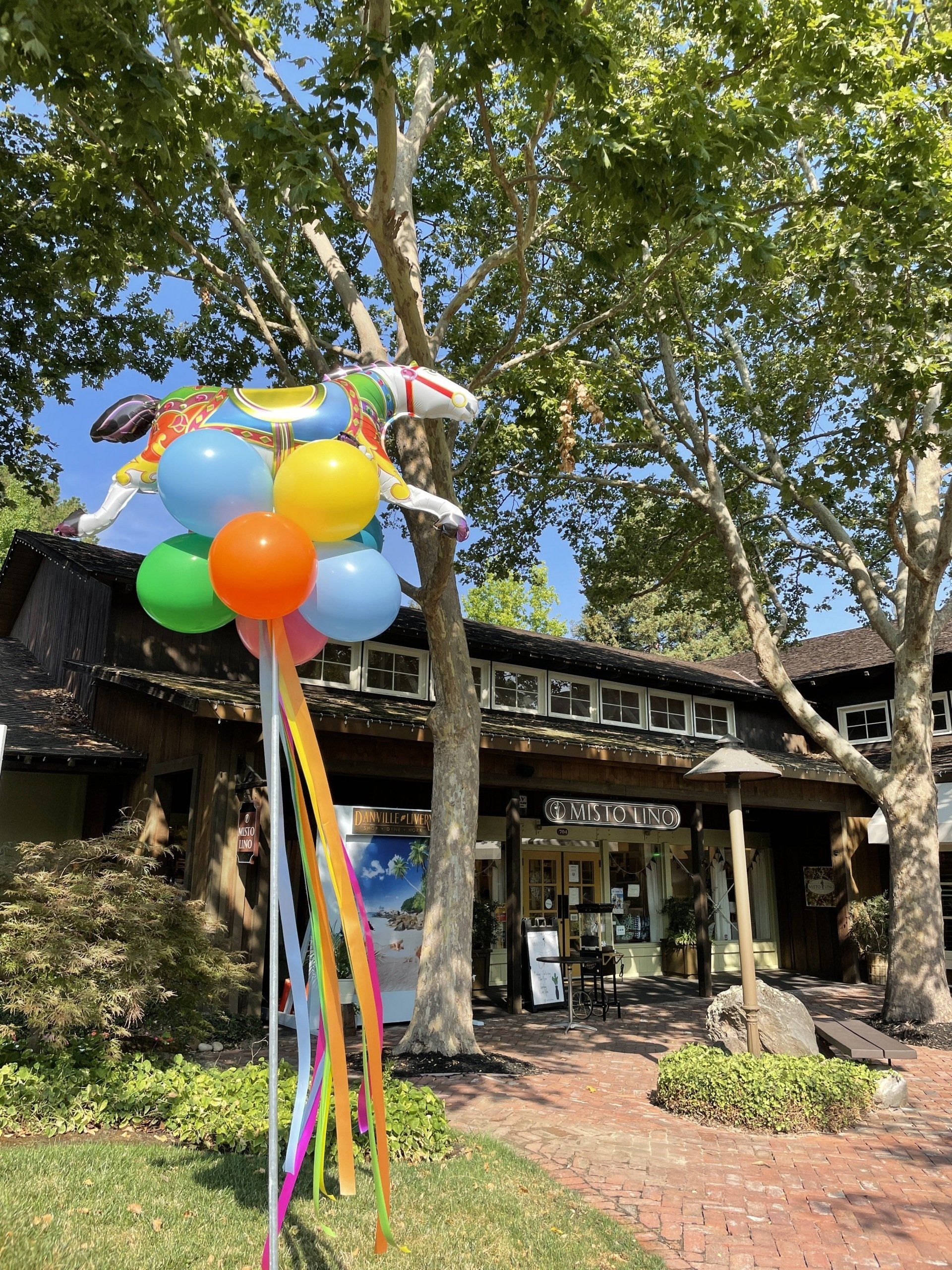 A bunch of balloons are hanging from a tree in front of a building.