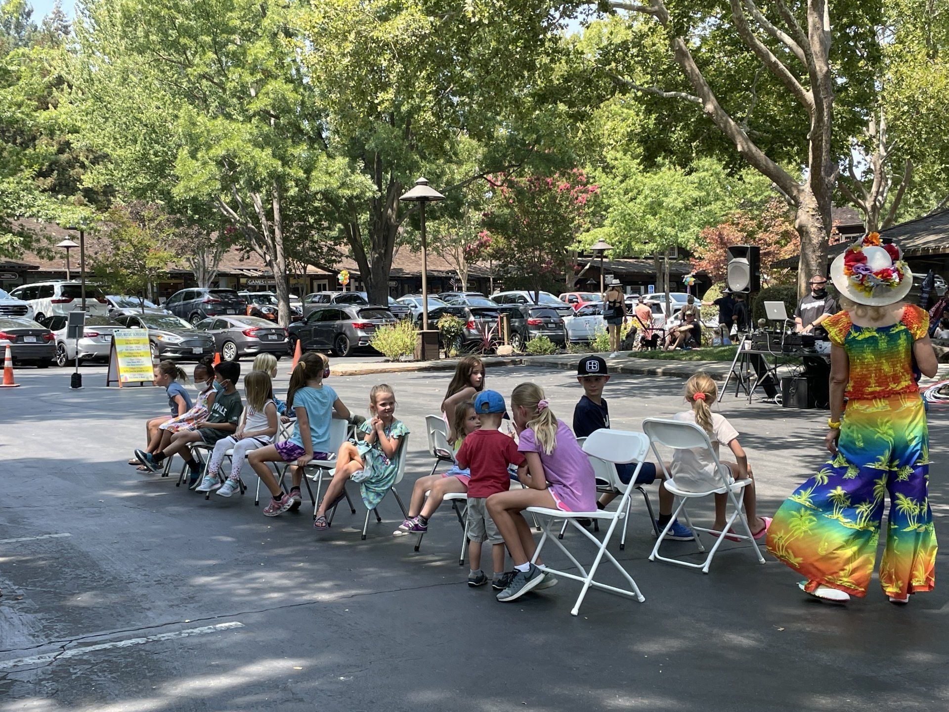 A group of children are sitting in chairs in a parking lot.