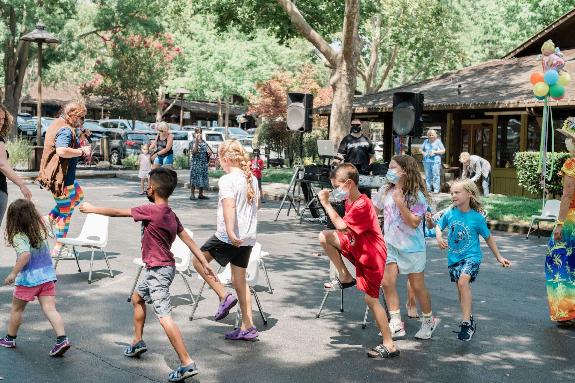 A group of children are dancing in a park with a clown.