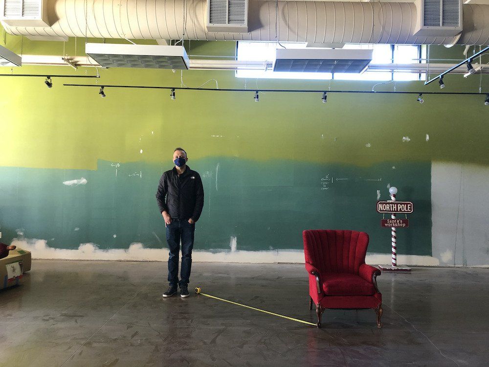 A man wearing a mask is standing next to a red chair in an empty room.