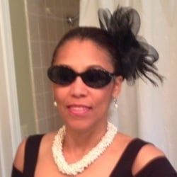 A woman wearing sunglasses and a pearl necklace is standing in front of a shower curtain.