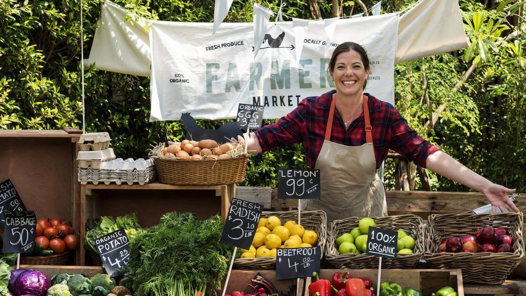 A woman is standing in front of a fruit and vegetable stand.