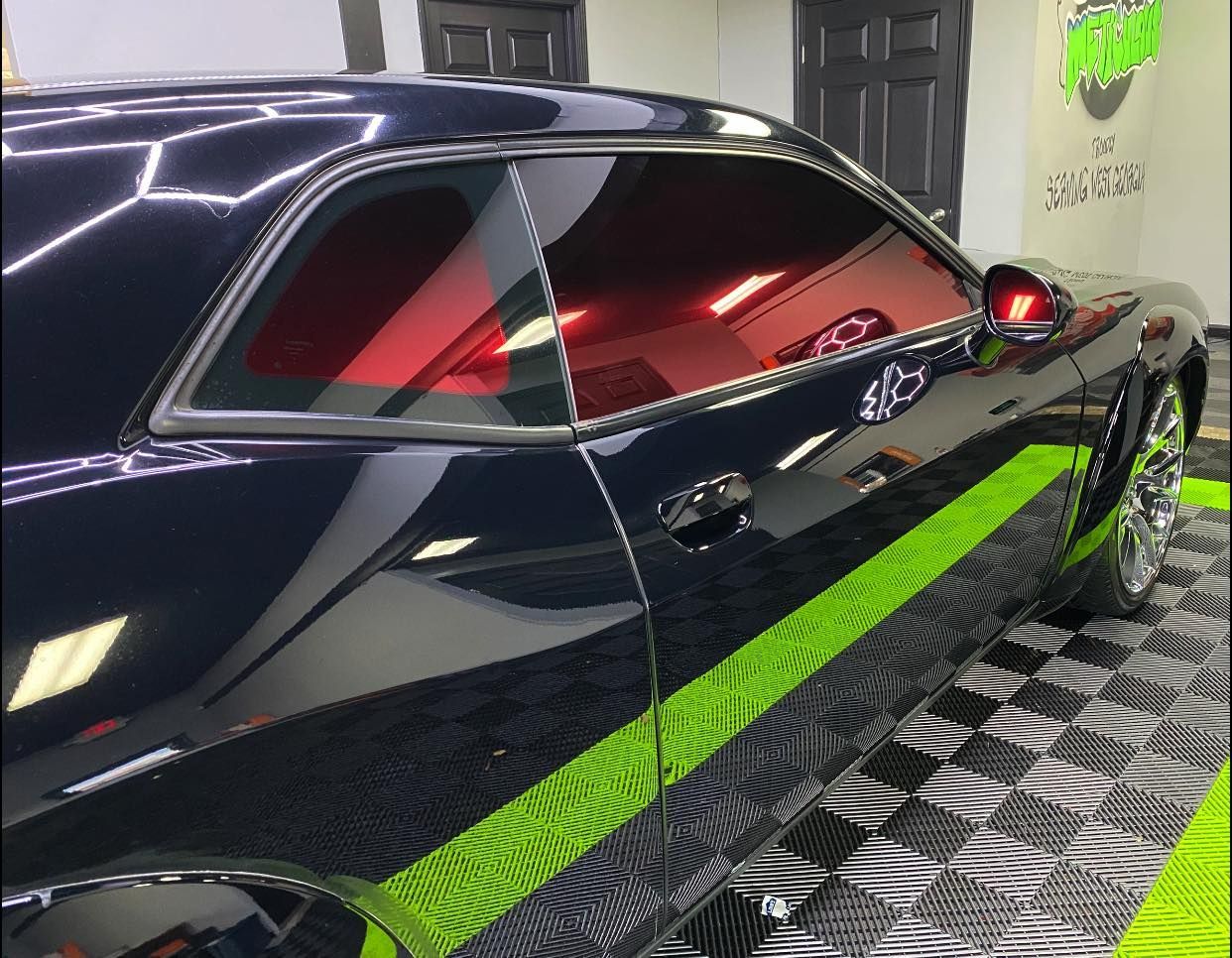 A black car is parked on a green mat in a garage.