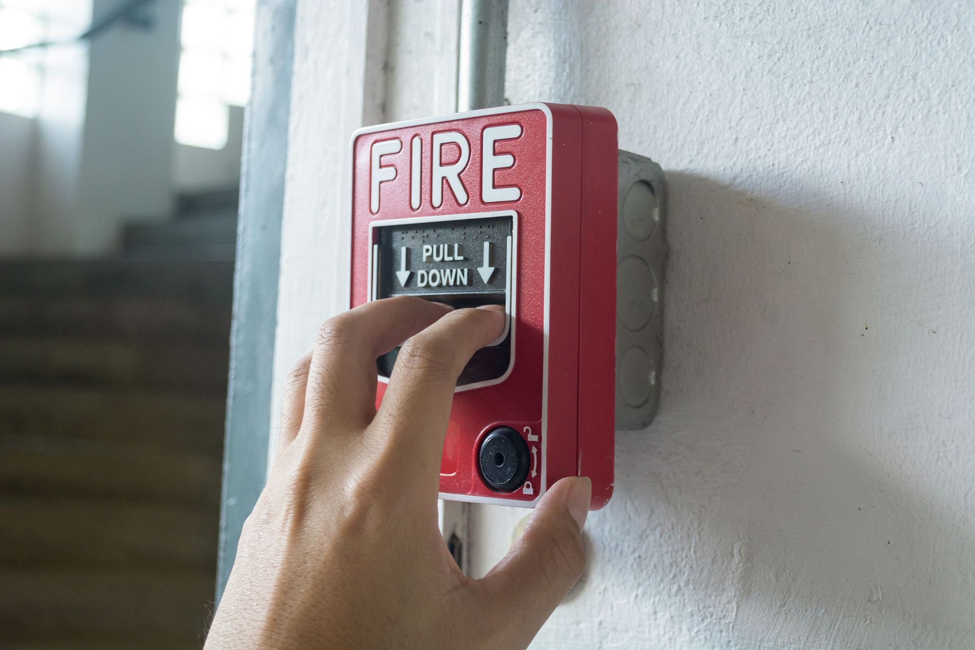 An individual pressing a fire alarm button during fire safety systems maintenance.
