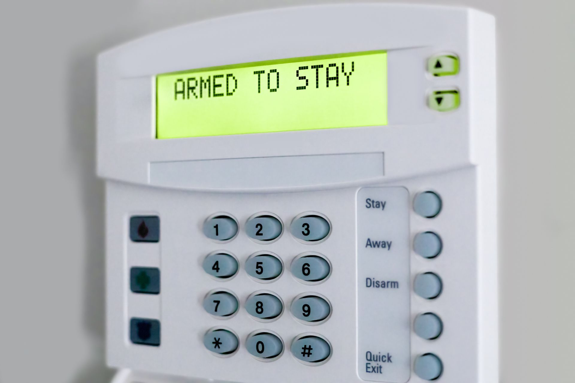 A home security keypad with 'ARMED TO STAY' on screen, showing number and control buttons.