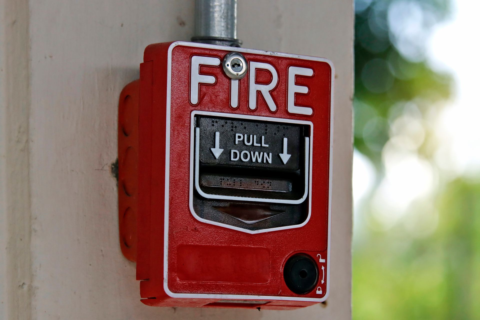 Red fire alarm box, part of the security system, mounted on a concrete wall outside the property.