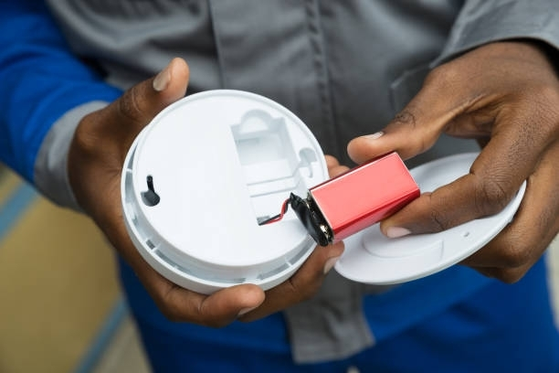 Professional electrician safely disconnecting battery from home security alarm panel for repair.