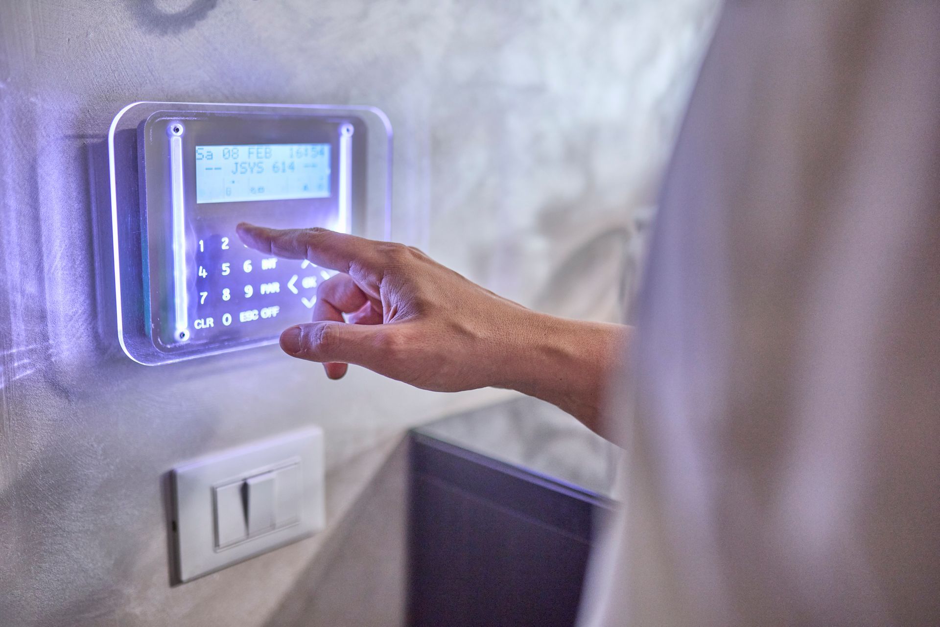 A man is setting up an illuminated modern home security keypad near the entrance door.