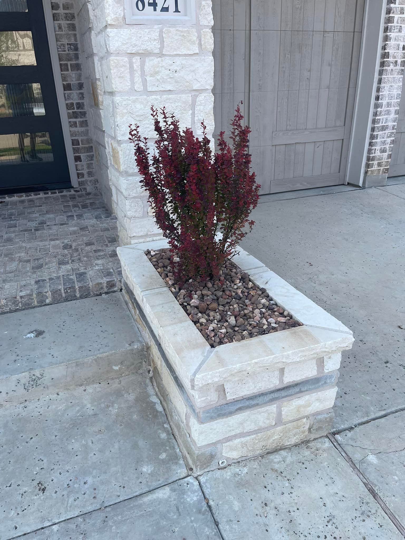 A brick planter with a plant in it is on the sidewalk in front of a brick building.