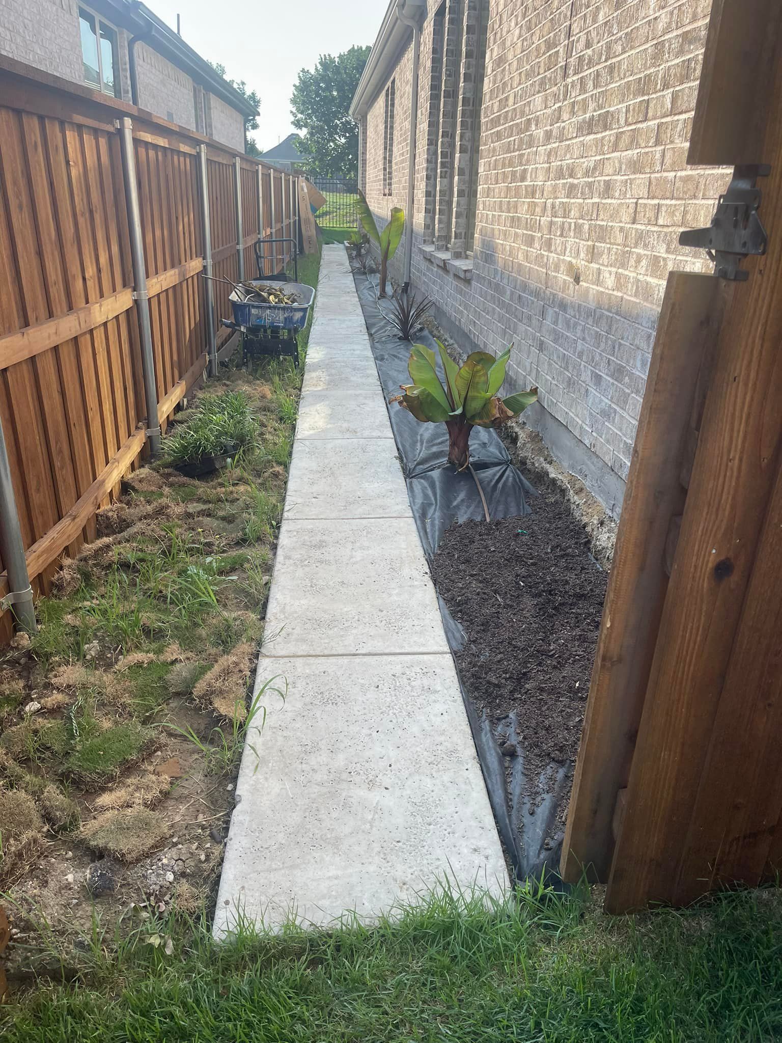 A sidewalk leading to a house next to a wooden fence.