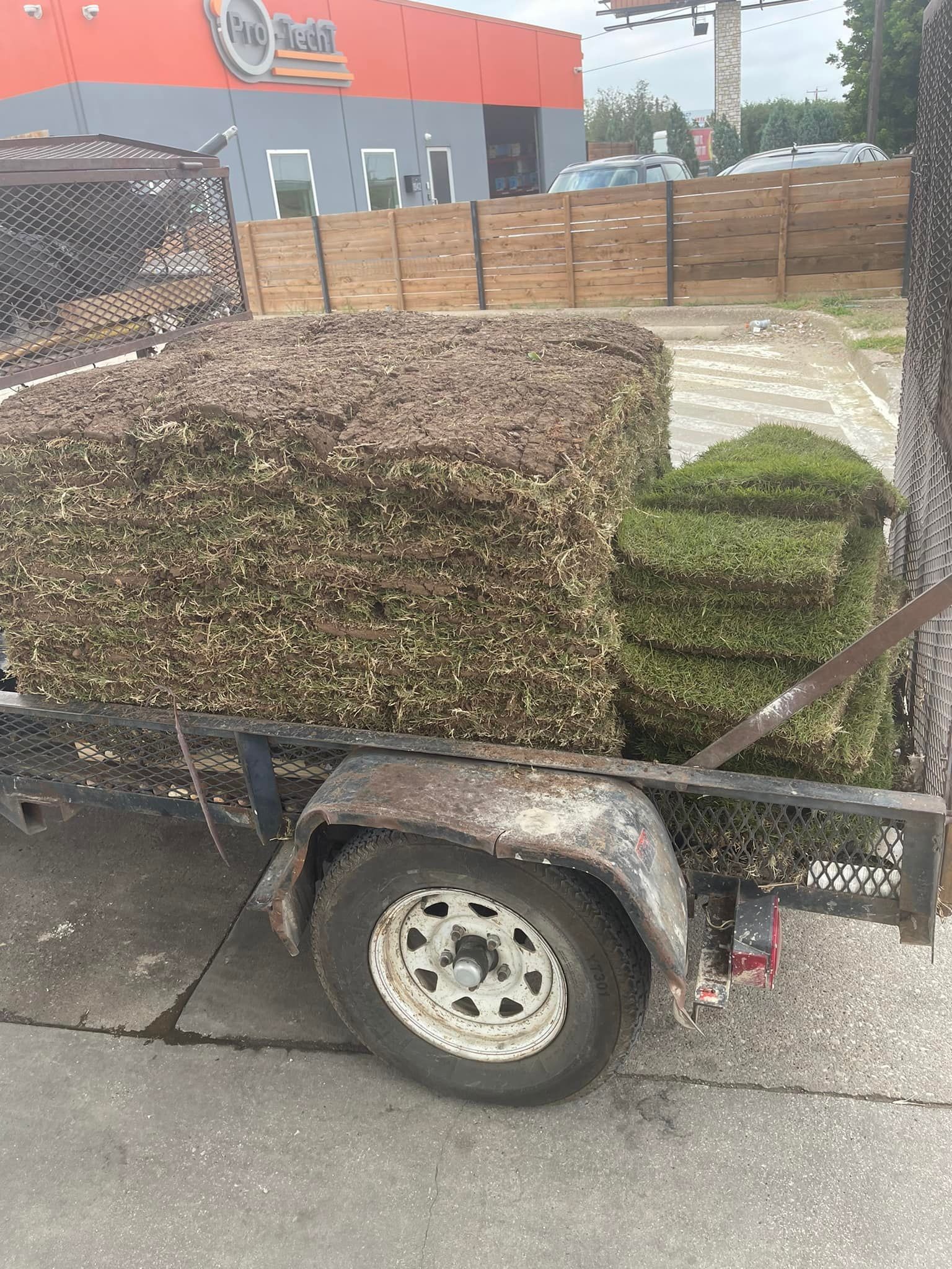 A trailer filled with bales of grass is parked on the side of the road.