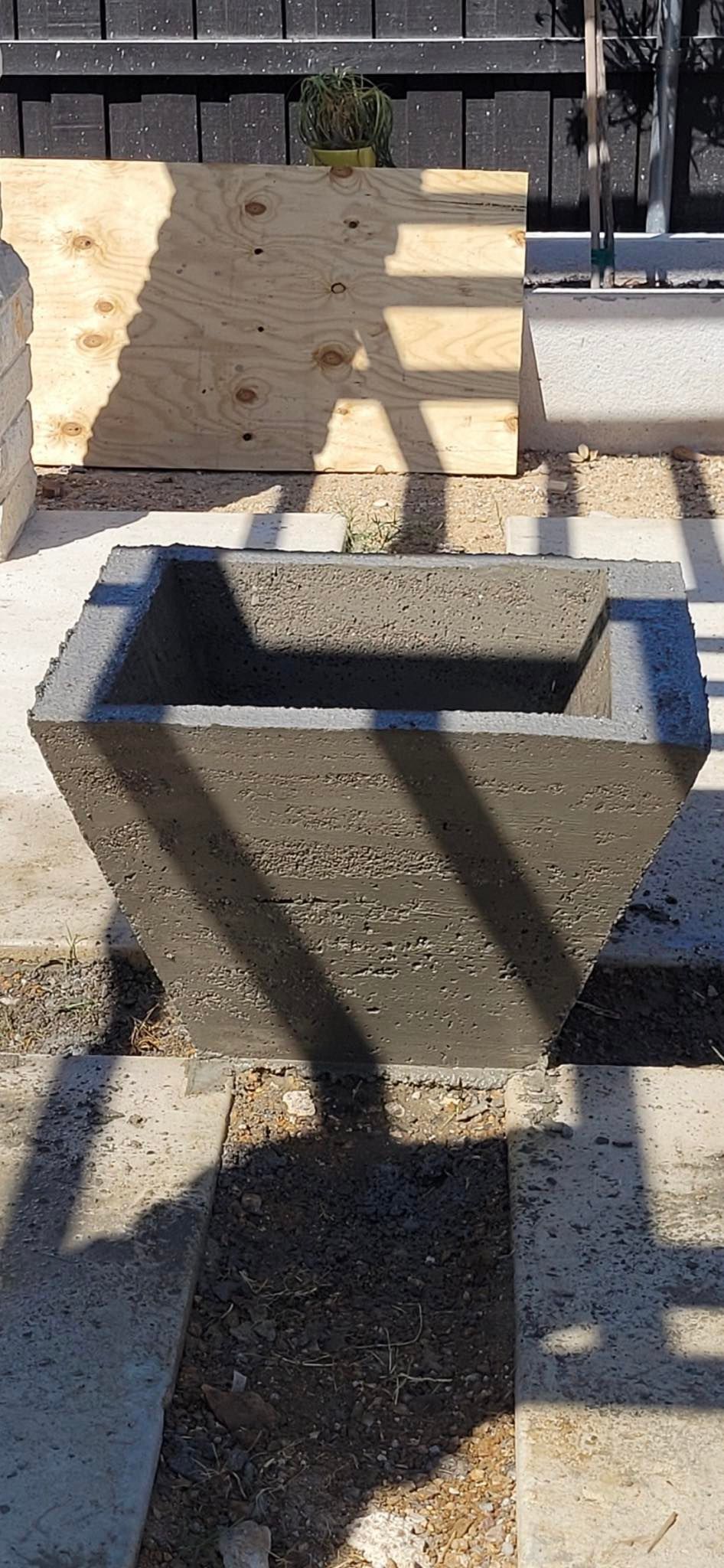 A concrete planter is sitting on a sidewalk next to a wooden fence.