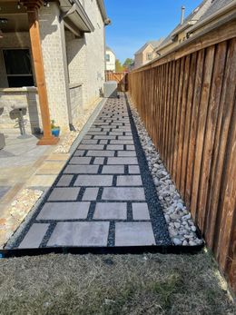 A stone walkway leading to a house next to a wooden fence.