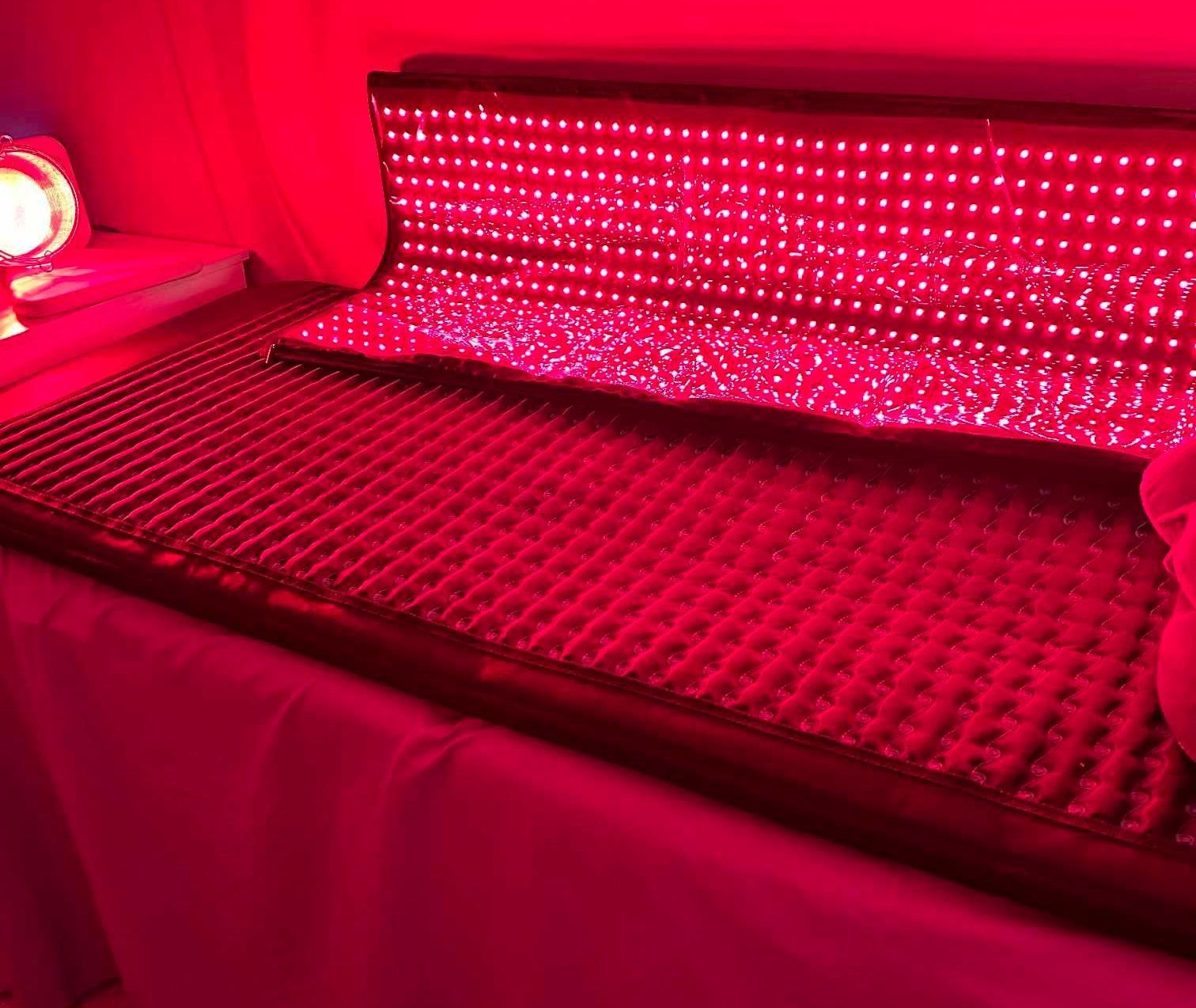 Red light therapy bed with a grid of red lights, set on a table covered with white fabric.