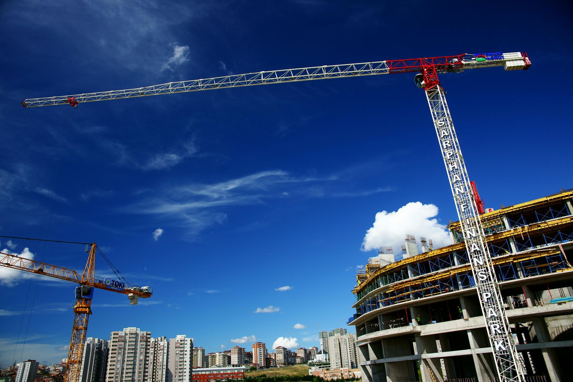 Construction cranes against a bright blue sky, working on a building in a city.