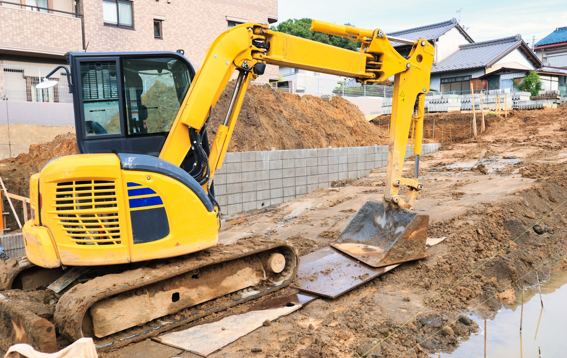 Yellow excavator digging in a construction site with houses in the background.