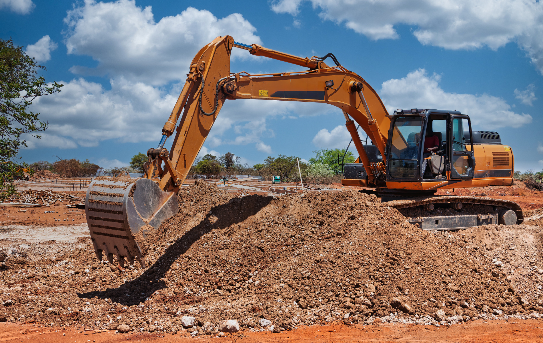 Orange excavator digging dirt at a construction site on a sunny day.
