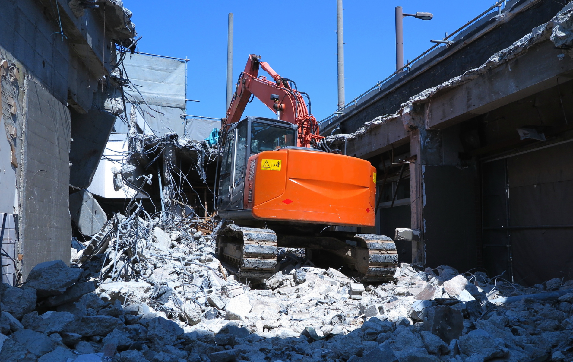 Orange excavator demolishing a building; rubble covers the ground.