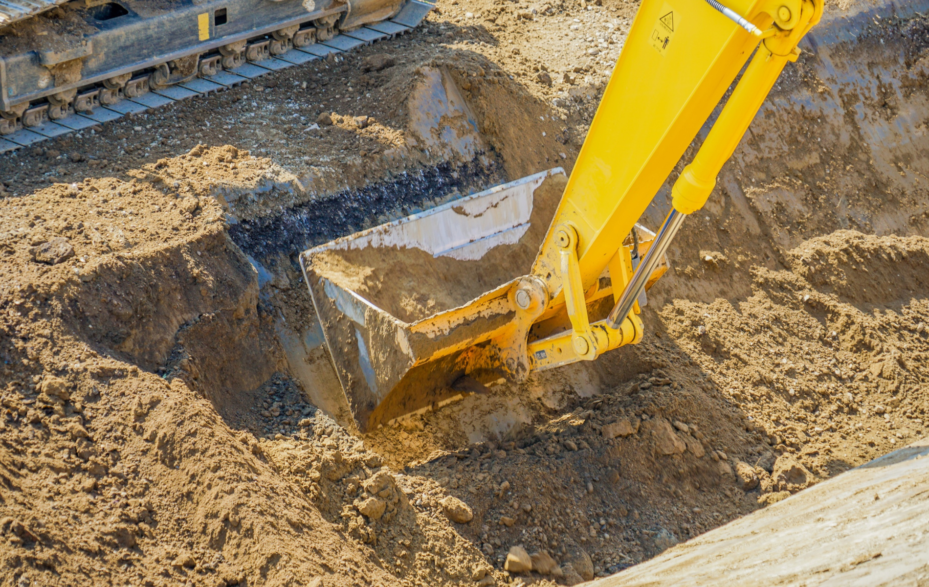 Yellow excavator digging in brown dirt.