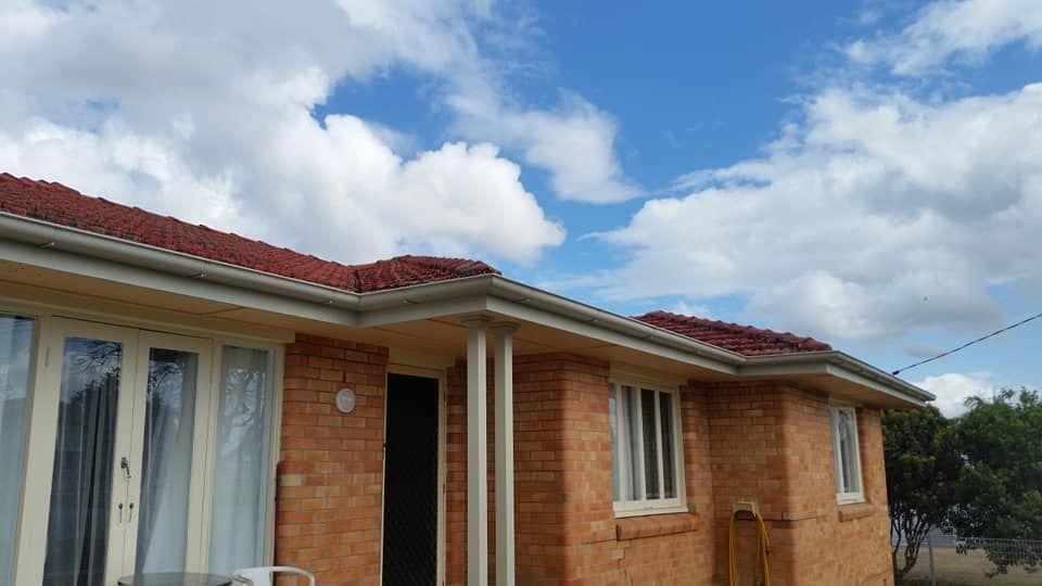 A Brick House With A Red Roof And White Windows On A Sunny Day — House Guttering Pty Ltd In Bauple, QLD