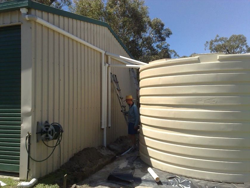 A Man With A Ladder Standing Next To A Water Tank — House Guttering in Bauple, QLD