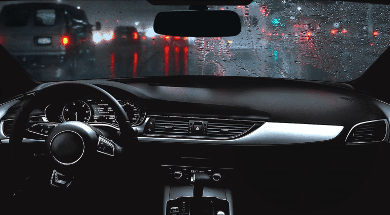 Interior car view, driving in the rain at night. Street lights and car lights reflect on wet windshield.