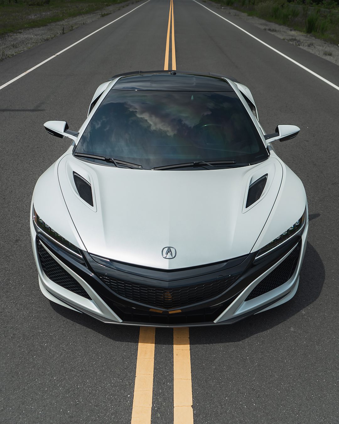 White Acura NSX sports car on a paved road with double yellow lines, top-down view.