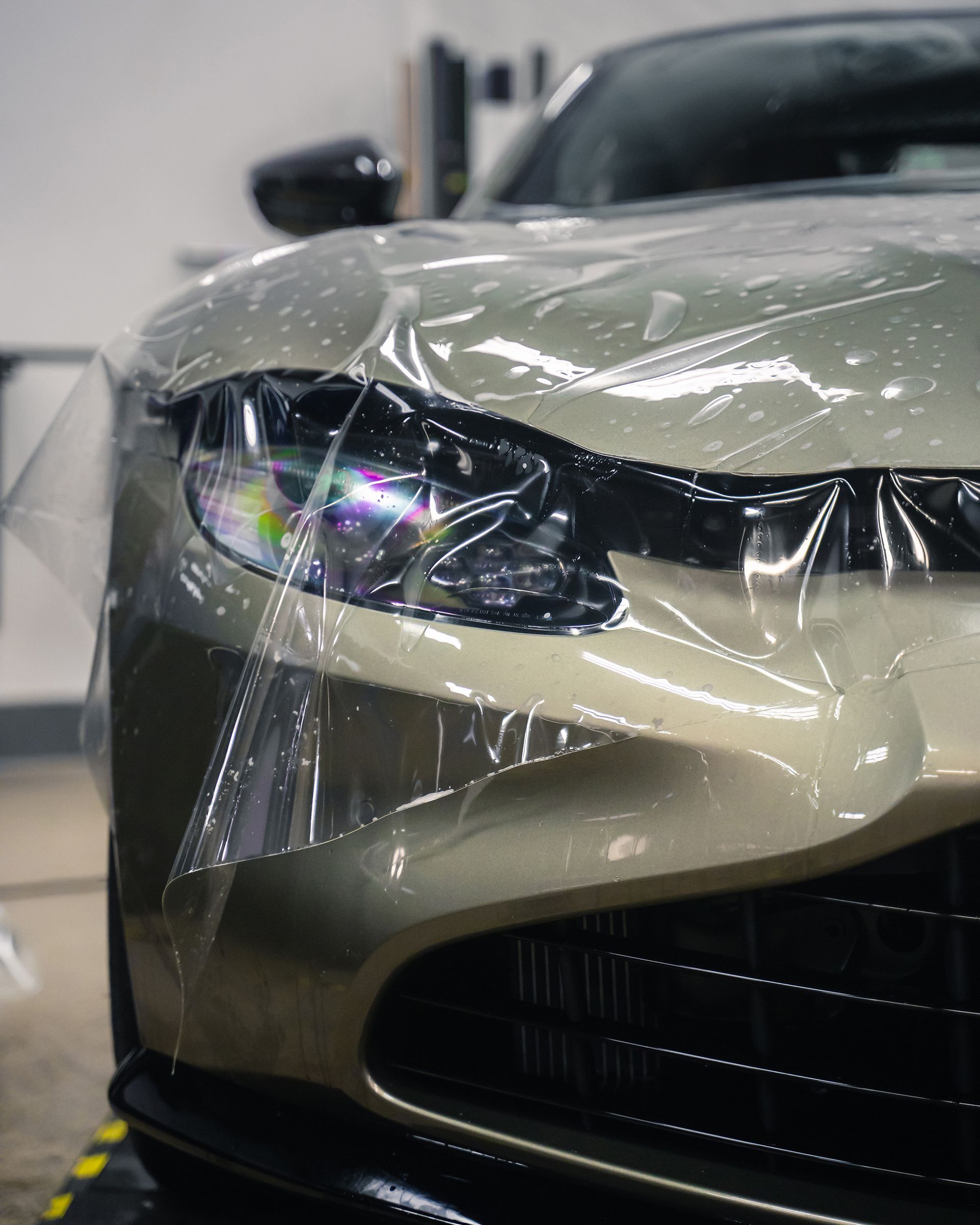A car's front end with protective film applied, headlights and black grill visible.