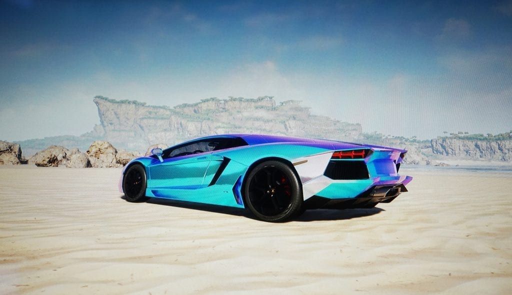 A blue Lamborghini Aventador on a sandy plain with rock formations and a bright sky in the background.