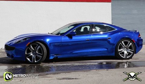 Blue Fisker Karma car parked in front of a white building with a red stripe.