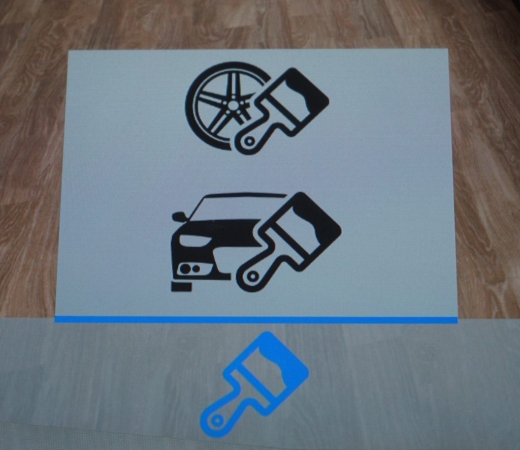A paper with car and wheel icons each paired with a paintbrush, plus a paintbrush below, on a wooden surface.
