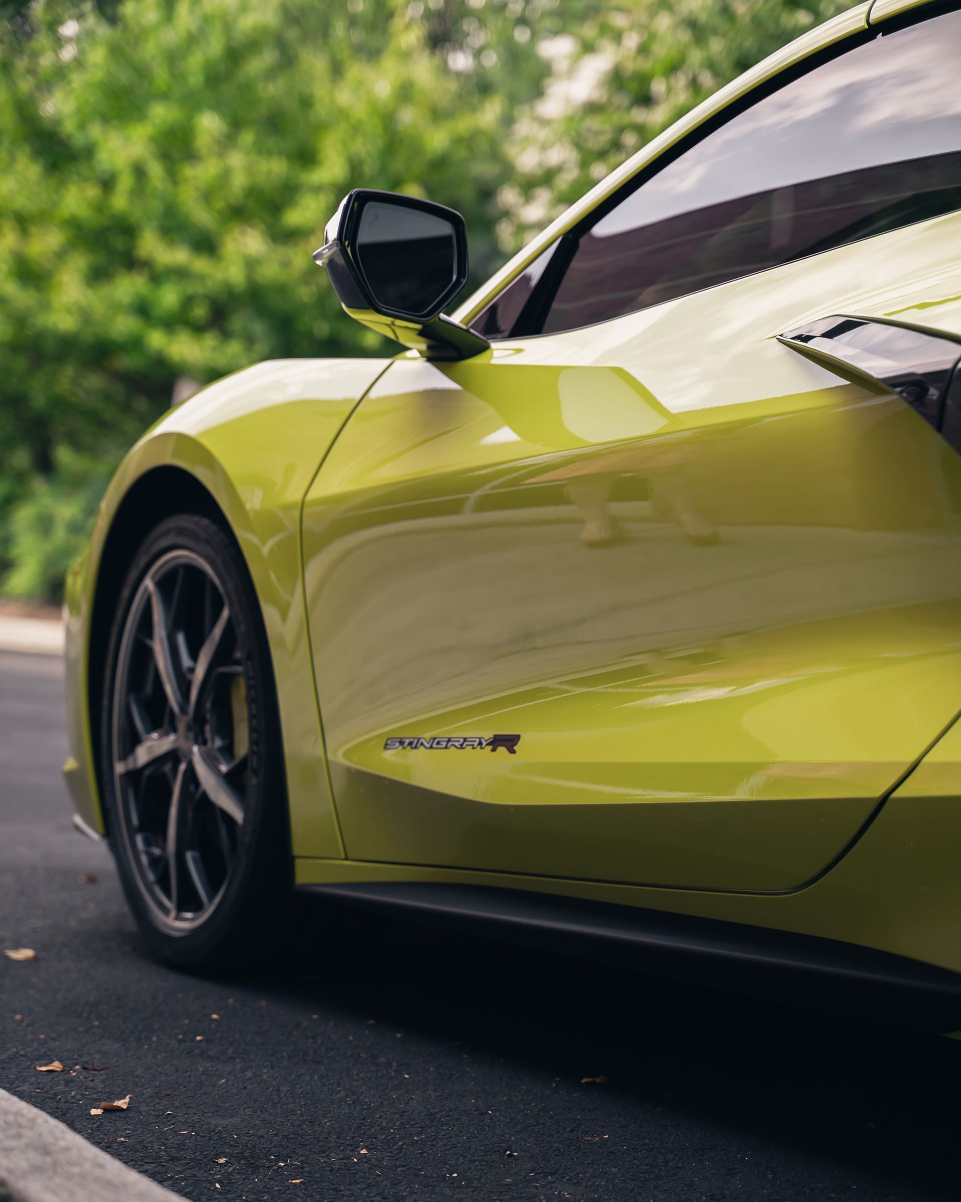 Yellow sports car parked on asphalt next to greenery, with details including side view mirror and wheel.